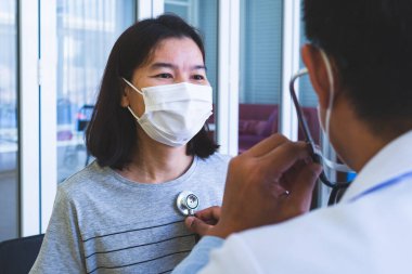Hastalık için hastaneye gelen kadın hastayı muayene etmek için steteskop kullanan Asyalı doktor. Sağlık ve Tıp Konsepti