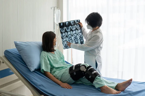 orthopedist shows magnetic resonance imaging or MRI of knee to asian patient that has knee injury from sport trauma. healthcare and medical concept