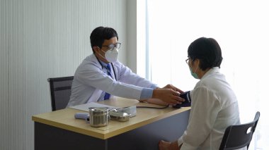 Asyalı doktor hipertansiyon nedeniyle hastaneye gelen yaşlı kadın hastanın tansiyonunu ölçmek için otomatikleştirilmiş sfenometre kullanıyor. Sağlık ve Tıp Konsepti