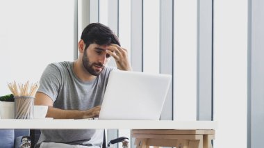 Ciddi yüzlü, genç, yakışıklı, beyaz bir adam evden bilgisayar kullanarak çalışıyor. iş ve teknoloji kavramı