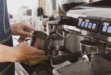 Genç adam köpüklü süt yapmak için kahve makinesi kullanıyor. barista ve kafe konsepti