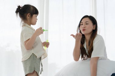Asyalı anne yazın küçük kızıyla oturma odasında baloncuk üfleme oyunu oynuyor. aile ve ilişki