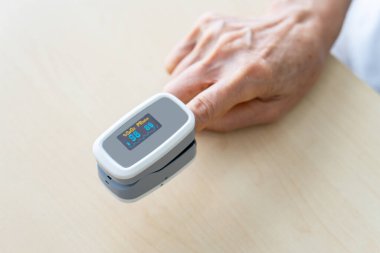 Yaşlı kadın oksijen doygunluğunu nabız ölçer makinesiyle ölçüyor ve hastane kliniğinde normal değerini gösteriyor. Sağlık ve Tıp Konsepti