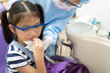 Dişçi asistanı diş ameliyatından sonra genç kızın ağzını temizlemesine yardım ediyor. Diş hekimliği ve sağlık hizmeti kavramı