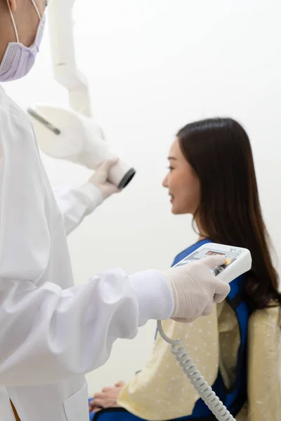 dentist assistant using x-ray machine to scan tooth of young asian woman in clinic. dentistry and healthcare concept
