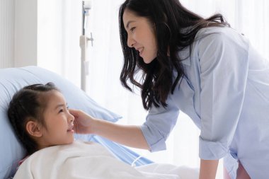 Asyalı anne hasta, ateşi olan ve hastanenin pediyatri koğuşunda yatan kızına bakıyor. Sağlık ve Tıp Konsepti
