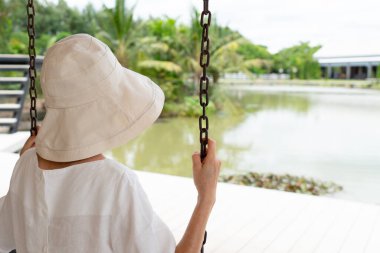 Bir salıncakta oturan, bahçeye ve göle bakan yaşlı kadının dikiz aynasından.