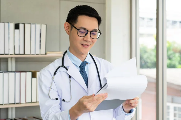 young asian doctor in white coat with serious face reading lab result of patient. healthcarea and medical concept