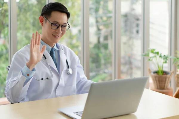 young asian doctor wearing headphone and using computer to give consult to the patient via video call in the hospital office. telemedine and healthcare concept