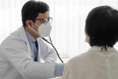 Asyalı doktor, hastaneye hastalık için gelen hastayı muayene etmek için steteskop kullanıyor. Sağlık ve Tıp Konsepti