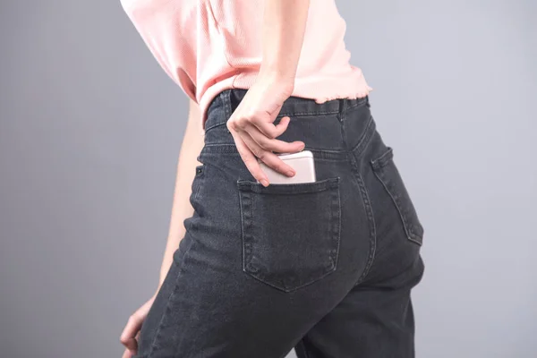 phone on woman jeans pocket on grey background