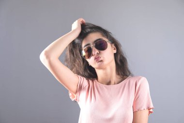 Mutlu kadın gri arka planda güneş gözlüğü takıyor.