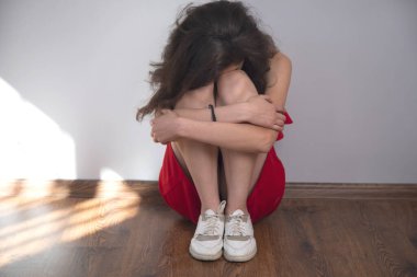 Üzgün kadın, oda zemininde oturuyor.