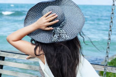 Kadın deniz arka planında bankta oturuyor.