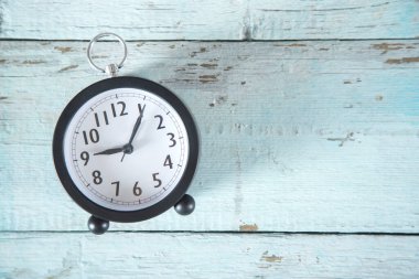 Mavi ahşap masada siyah saat.