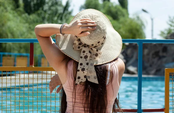 Havuzun yanındaki şapkalı kadın.