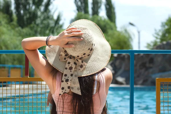 Havuzun yanındaki şapkalı kadın.