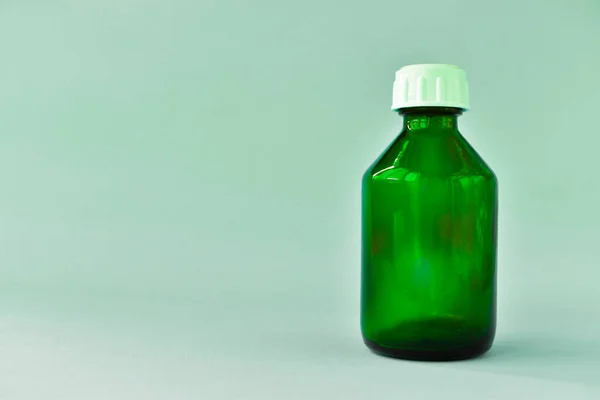 A green glass bottle for cosmetics, natural medicine, essential oils or other liquids isolated on a light background in the center looks straight.