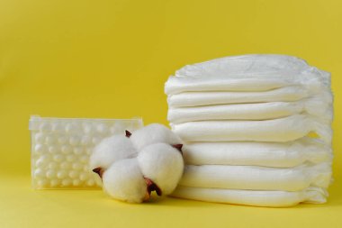 Sarı arka planda kuru pamuklu bebekler için beyaz bebek bezi ve pamuk tomurcukları var. Organik ürünler.