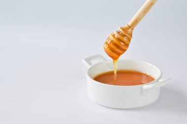 Bal, ahşap bir kaşıktan akarak beyaz arka plandaki bir kaseye akar. Minimalizm.