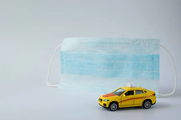 Miniature of a yellow taxi car on the background of a blue medical mask. Minimalism. Safe transport