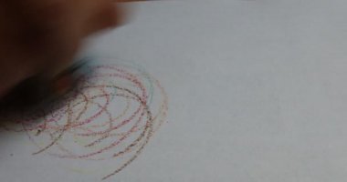 El, beyaz kağıda renkli kalemlerle soyut bir çiçek çizer.