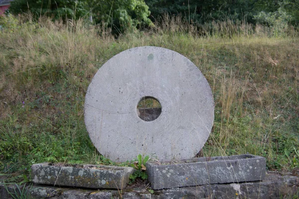 heavy stone mill wheel stands in the grass
