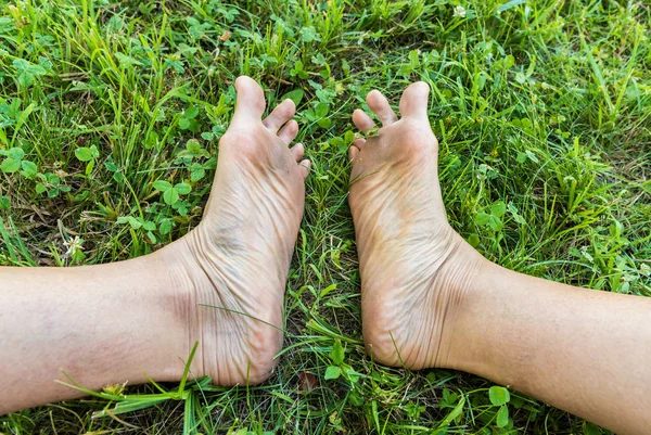 Dirty soles of the adult feet on the green grass.