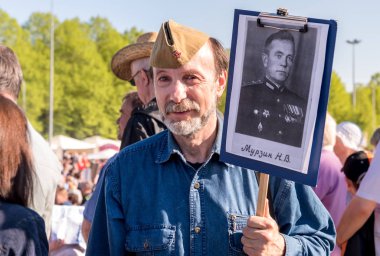 Riga, Latvia - May 9, 2018: Elderly bearded man with a portrait of his relative in Immortal Regiment on annual Victory Day in the Victory park of Riga, Latvia clipart