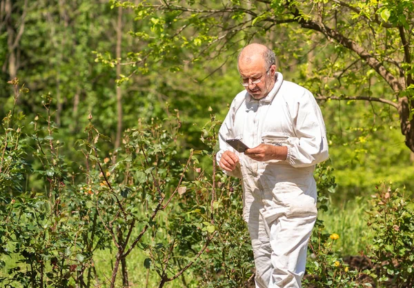 Senior man in white dress with phone in hand in the garden.