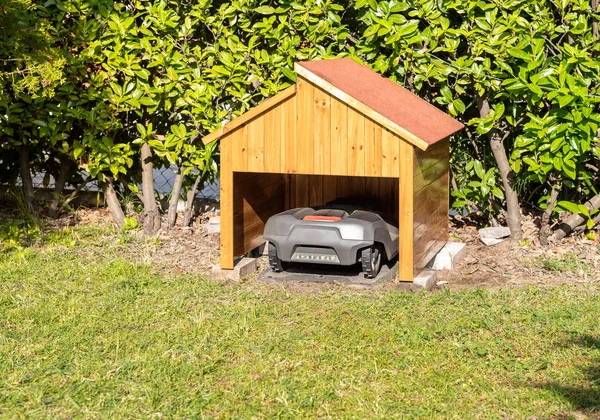 Ahşap garajda korunan şarj istasyonunda Robotik Çim Biçme Makinesi park.
