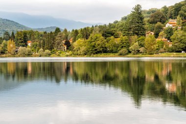 Bir sonbahar gününde bulutların ve ağaçların yansımaları ile Ghirla Gölü Manzara, Varese eyaleti, İtalya