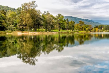 Bir sonbahar gününde bulutların ve ağaçların yansımaları ile Ghirla Gölü Manzara, Varese eyaleti, İtalya