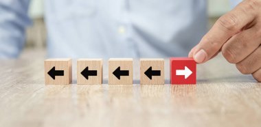 İş adamı eliyle, ok başlıklı küp tahta oyuncak bloğunu seçti. İkonlar, büyümeye ve başarıya liderlik eden iş dünyası kavramının zıt yönlerine işaret ediyor..