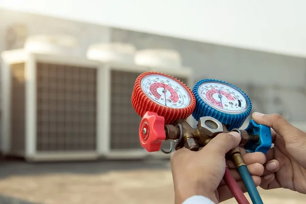 Endüstriyel fabrika klimalarını doldurmak ve dışarıdaki bakım hava kompresörü ünitesini kontrol etmek için basınç göstergesi ölçüm cihazı kullanan hava tamircisi..