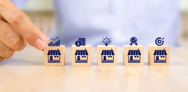 Kapalı çekimde, bayilik mağazası ikonu ile aynı hizaya gelen tahta oyuncak bloklarını seçin. Finansal pazarlama planlamasının küçük işletme büyümesi ve genişleme stratejisi için.