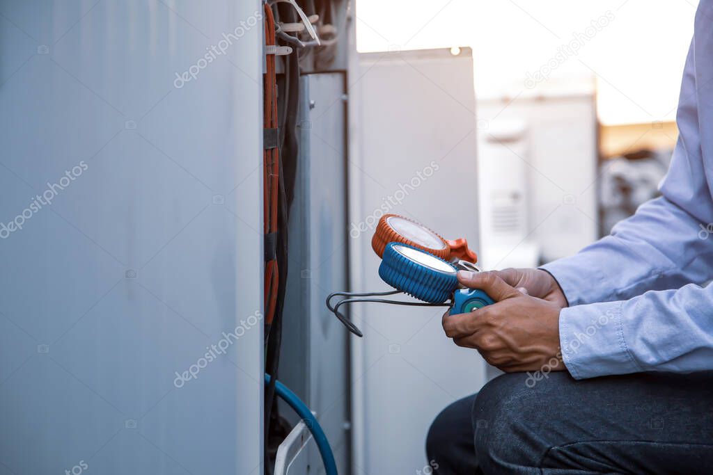 Air repair mechanic using measuring equipment for filling industrial factory air conditioners and checking maintenance outdoor air compressor unit.