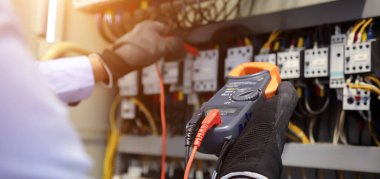 Elektrik mühendisi ana dağıtım panosundaki akım gerilimini kontrol etmek için dijital çoklu metre kullanıyor..