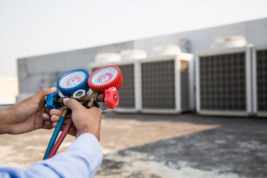 Hava onarım teknisyeni endüstriyel fabrika klimalarını doldurmak ve dış hava kompresörü ünitesini kontrol etmek için ölçüm ekipmanı kullanıyor..