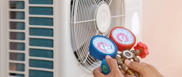 Air repair mechanic using measuring equipment for filling home air conditioner after cleaners and checking maintenance outdoor air compressor unit.