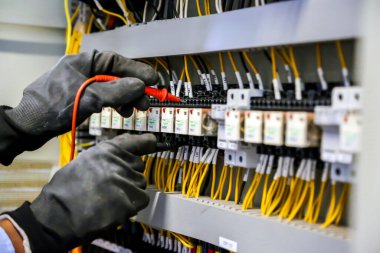Elektrik mühendisi, ana güç dağıtım panosundaki elektrik akımı voltajını kontrol etmek için dijital çoklu metre ölçüm ekipmanı kullanıyor..