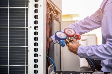 Hava onarım teknisyeni endüstriyel fabrika klimalarını doldurmak ve dış hava kompresörü ünitesini kontrol etmek için ölçüm ekipmanı kullanıyor..