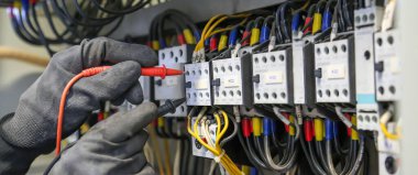Elektrik mühendisi, ana güç dağıtım panosundaki elektrik akımı voltajını kontrol etmek için dijital çoklu metre ölçüm ekipmanı kullanıyor..