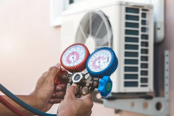 Air repair mechanic using measuring pressure gauge equipment for filling home air conditioner after cleaners and checking maintenance outdoor air compressor unit.