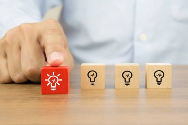 Küp tahta bloklardan ampul ya da lamba ikonları seçerken elinizi kapatın. İş dünyası liderliği ve yaratıcılığı için insan kaynakları kavramları.