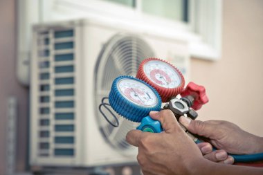 Hava onarım teknisyeni, temizleyicilerden sonra klimayı doldurmak ve dışarıdaki bakım hava kompresörü ünitesini kontrol etmek için basınç göstergesi ekipmanı kullanıyor..
