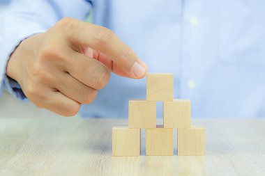 Yakın plan el, iş tasarımı konsepti için grafiksiz istiflenmiş bir küp şeklinde tahta blok oyuncağı ve çocuk vakfı uygulama becerileri için etkinlik seçin.