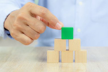 Yakın plan el, iş tasarımı konsepti için grafiksiz istiflenmiş bir küp şeklinde tahta blok oyuncağı ve çocuk vakfı uygulama becerileri için etkinlik seçin.