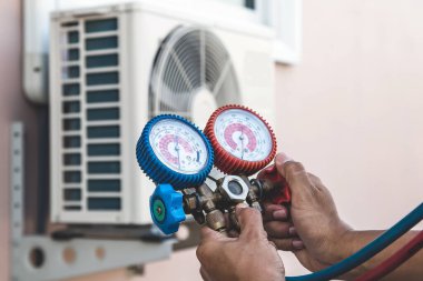 Hava onarım teknisyeni, temizleyicilerden sonra klimayı doldurmak ve dışarıdaki bakım hava kompresörü ünitesini kontrol etmek için basınç göstergesi ekipmanı kullanıyor..