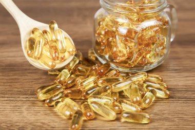 Tahta kaşıkta morina yağı kapsülü yığını. Sağlık hizmetleri kavramları için beslenme desteği.